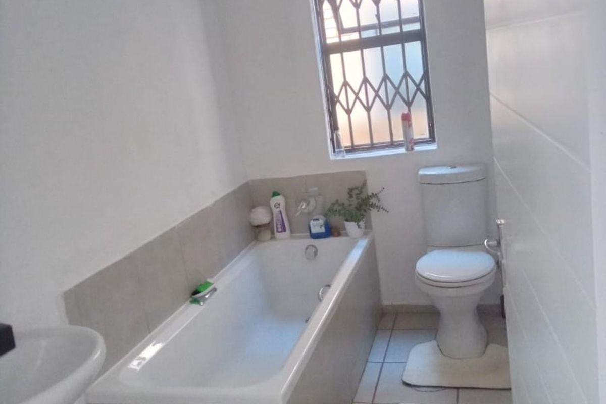 A functional bathroom featuring a built-in bathtub with tiled surround, a pedestal sink, and a toilet, complemented by a window with security bars.