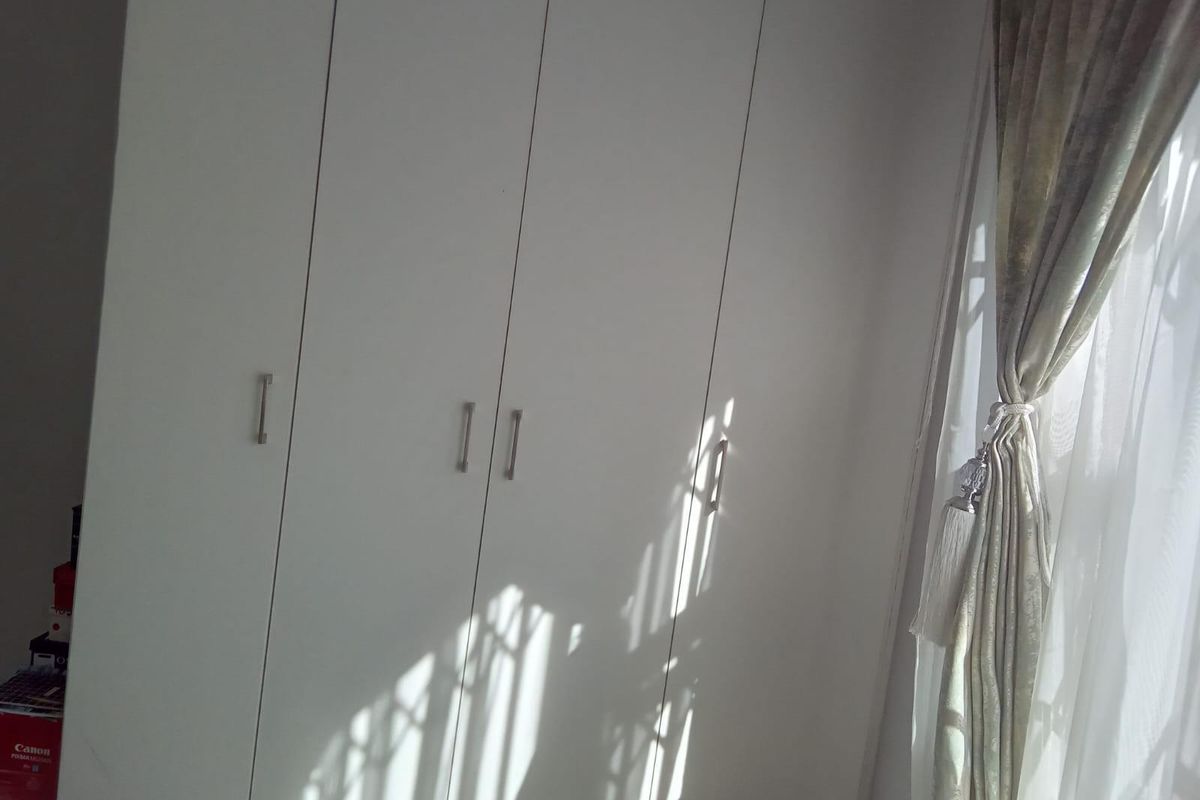 A bedroom featuring floor-to-ceiling built-in cupboards with modern handles, providing ample storage space.