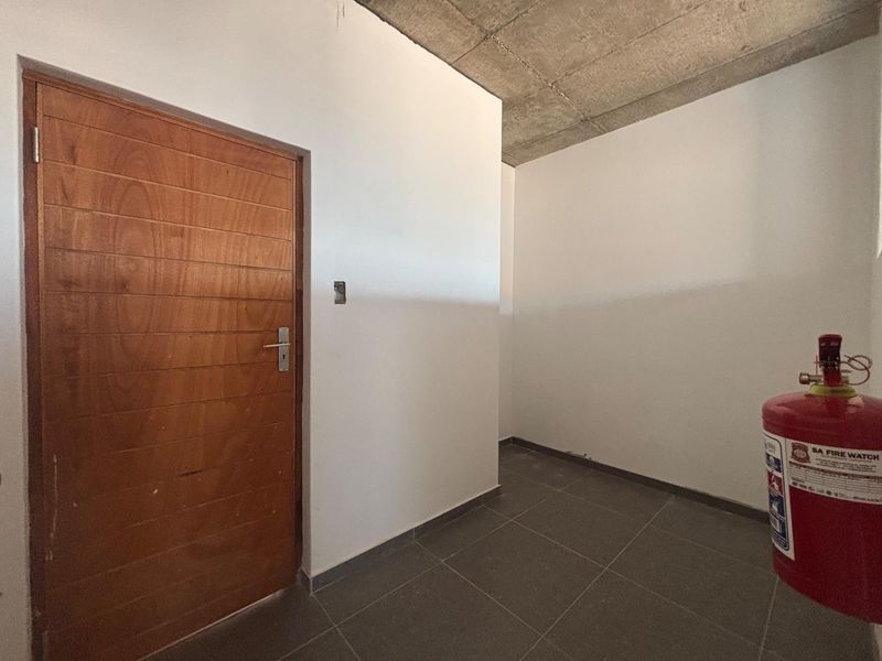 A minimalist office space featuring an exposed concrete ceiling, tiled flooring, and a solid timber door, presenting a clean, industrial-style blank canvas.