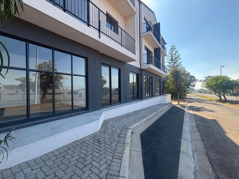 Modern office building exterior featuring large glass windows, metal balcony railings, and a clean paved walkway along the street frontage.