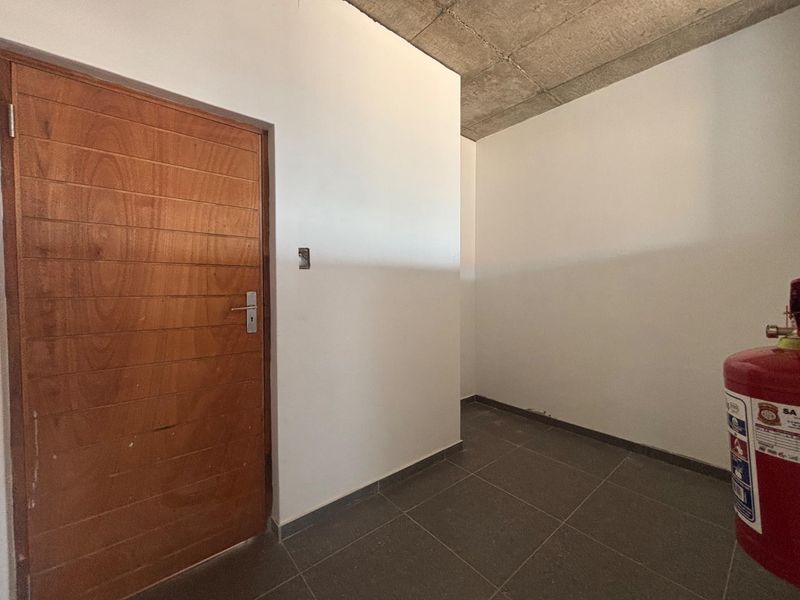 A minimalist office space featuring an exposed concrete ceiling, tiled flooring, and a solid timber door, presenting a clean, industrial-style professional environment.