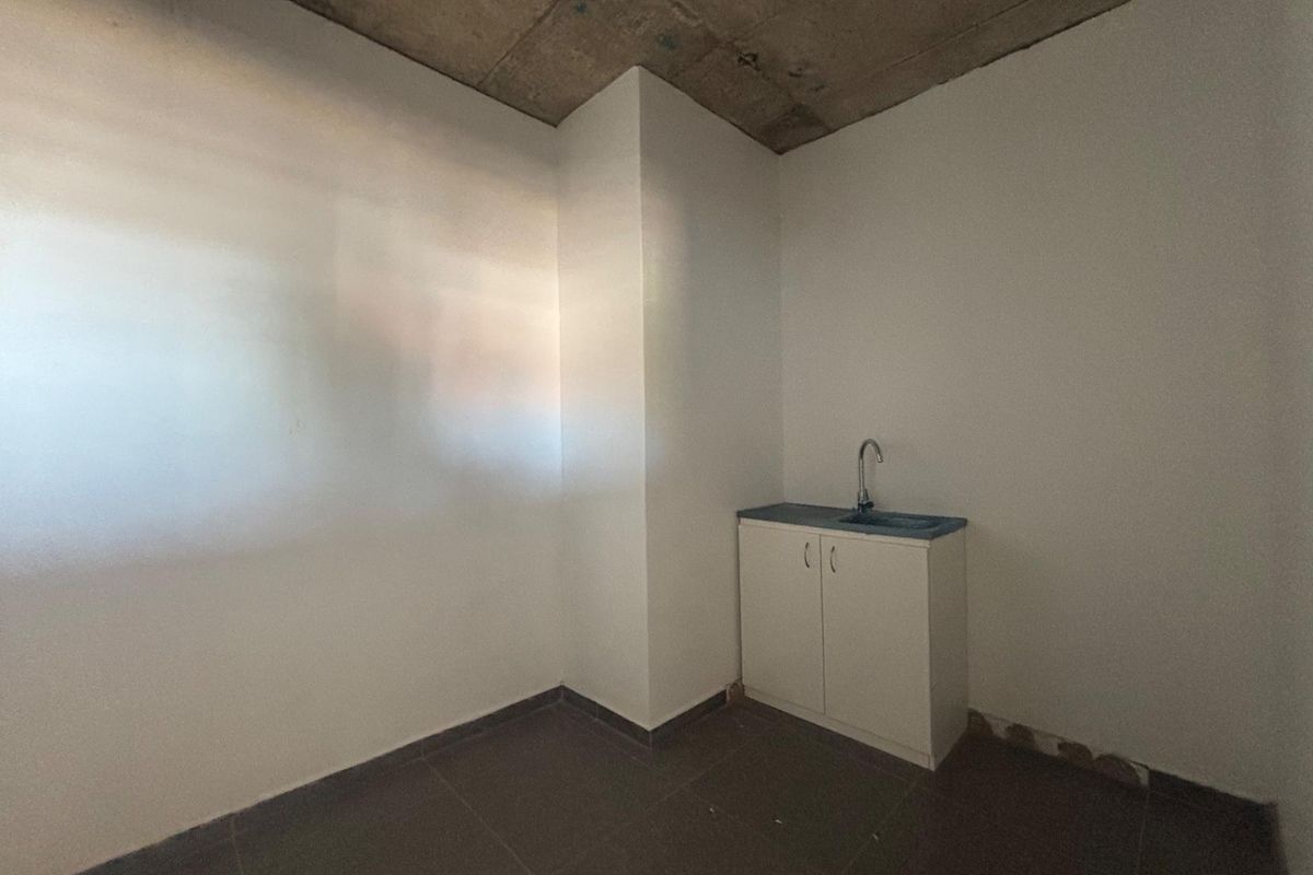 A compact, unfinished kitchenette area featuring a single sink, base cabinetry, tiled flooring, and an exposed concrete ceiling.