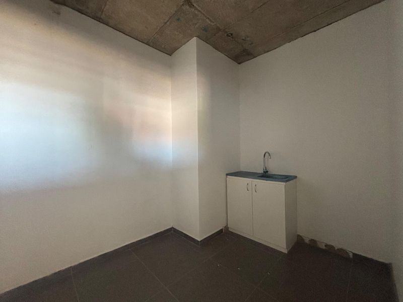 A compact, unfinished kitchenette area featuring a single sink, base cabinetry, tiled flooring, and an exposed concrete ceiling.