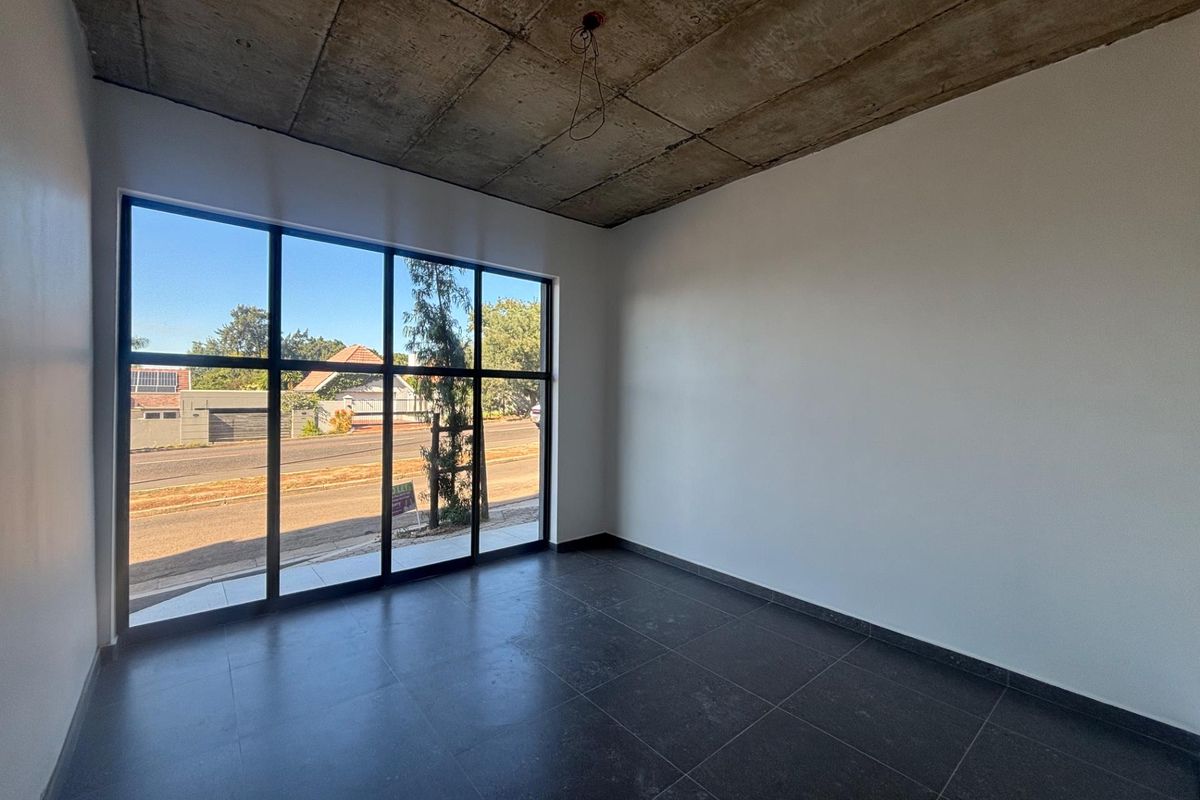 A bright, modern office space featuring large floor-to-ceiling windows, dark tiled flooring, and an industrial-style exposed concrete ceiling.