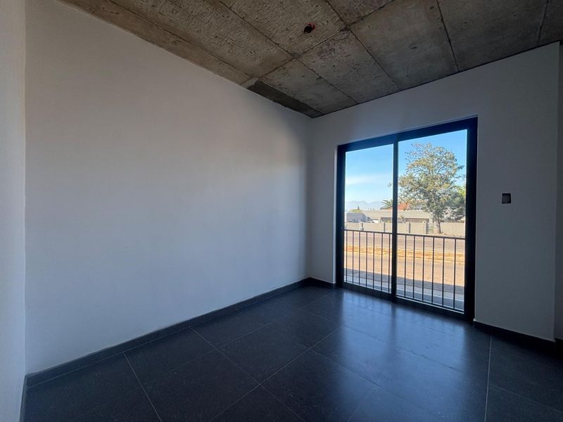 An empty office space featuring modern dark floor tiles, an exposed concrete ceiling, and a sliding glass door leading to a balcony.