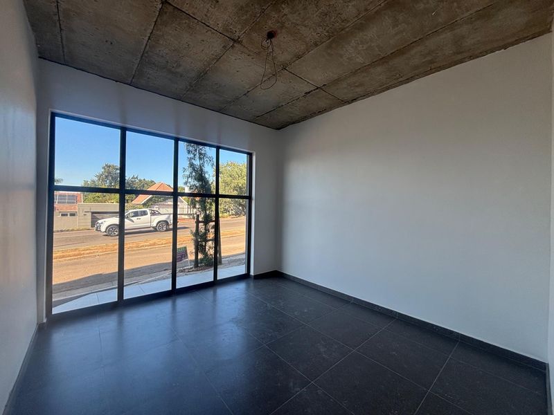 Modern empty office space featuring large floor-to-ceiling windows, exposed concrete ceiling, and dark tiled flooring, offering a clean and professional aesthetic.