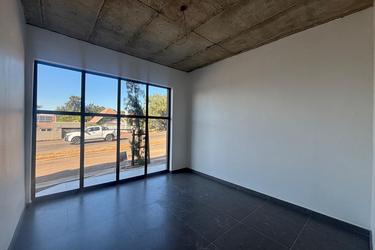 Modern empty office space featuring large floor-to-ceiling windows, exposed concrete ceiling, and dark tiled flooring, offering a clean and professional aesthetic.