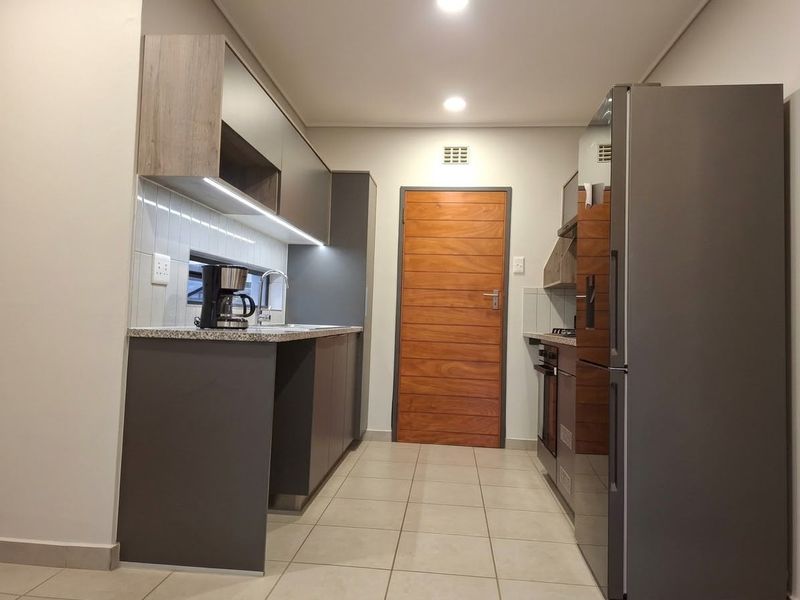 Modern galley-style kitchen featuring sleek grey cabinetry, stone countertops, integrated appliances, tiled backsplash, and recessed lighting.