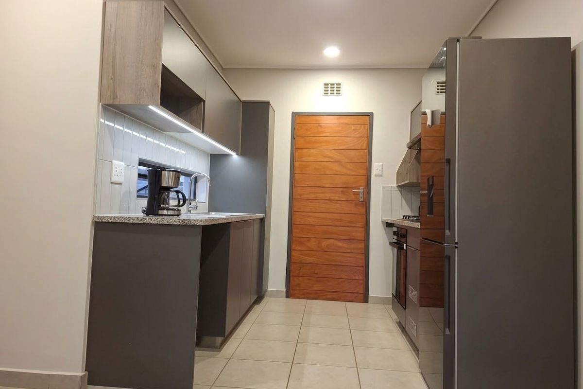 Modern galley-style kitchen featuring sleek grey cabinetry, stone countertops, integrated appliances, tiled backsplash, and recessed lighting.