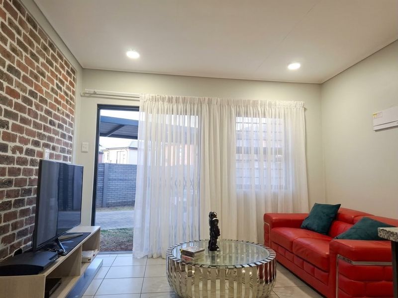 A modern living room featuring an exposed brick accent wall, tiled flooring, recessed lighting, and direct access to the outdoor area via a sliding door.