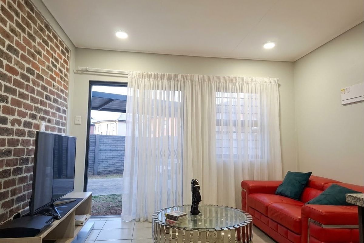 A modern living room featuring an exposed brick accent wall, tiled flooring, recessed lighting, and direct access to the outdoor area via a sliding door.