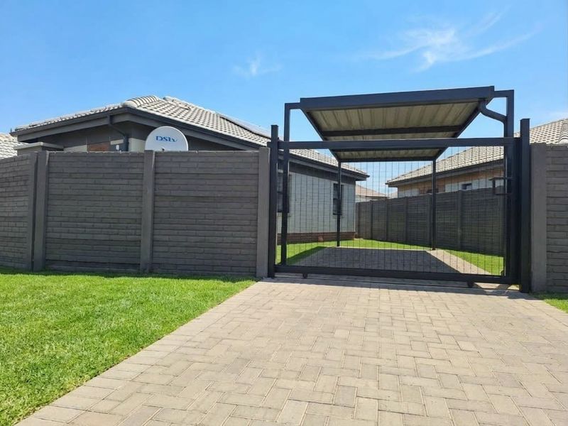 Front exterior view featuring a paved driveway, secure sliding gate, and a covered carport structure with brick boundary walling.