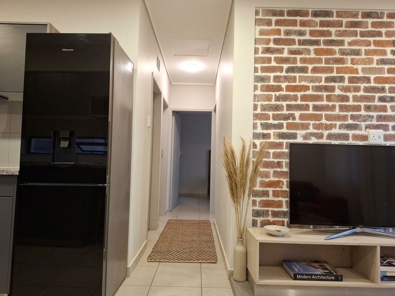 A well-maintained hallway featuring a decorative exposed brick wall, neutral tiled flooring, and clean finishes leading to adjacent rooms.