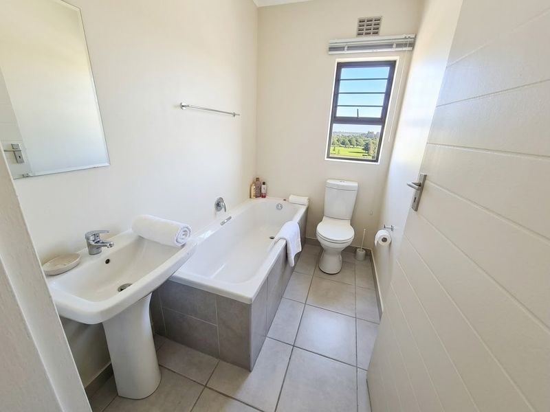 A clean and functional bathroom featuring a pedestal basin, built-in bathtub, and toilet with neutral tiled flooring and natural light.