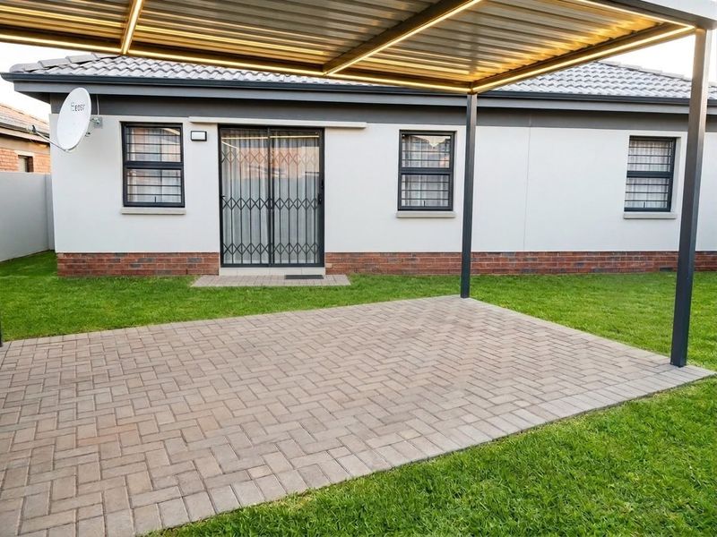 A well-maintained paved patio area featuring a modern metal pergola, providing a clean outdoor space adjacent to the rear of the house.