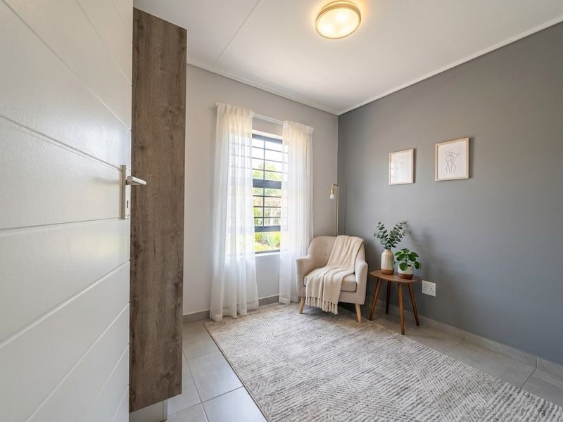A well-maintained bedroom featuring neutral tiled flooring, a modern grey accent wall, and natural light through a window with security bars.
