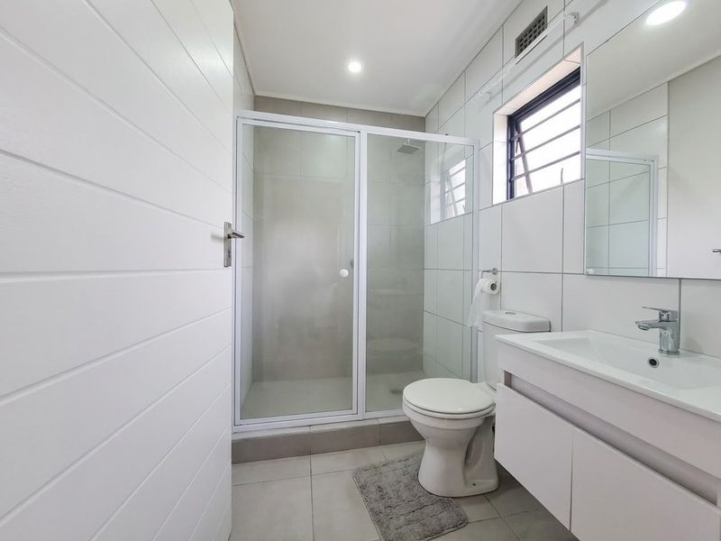 A clean, modern bathroom featuring a glass-enclosed shower, wall-mounted vanity with basin, and neutral tiled finishes throughout.