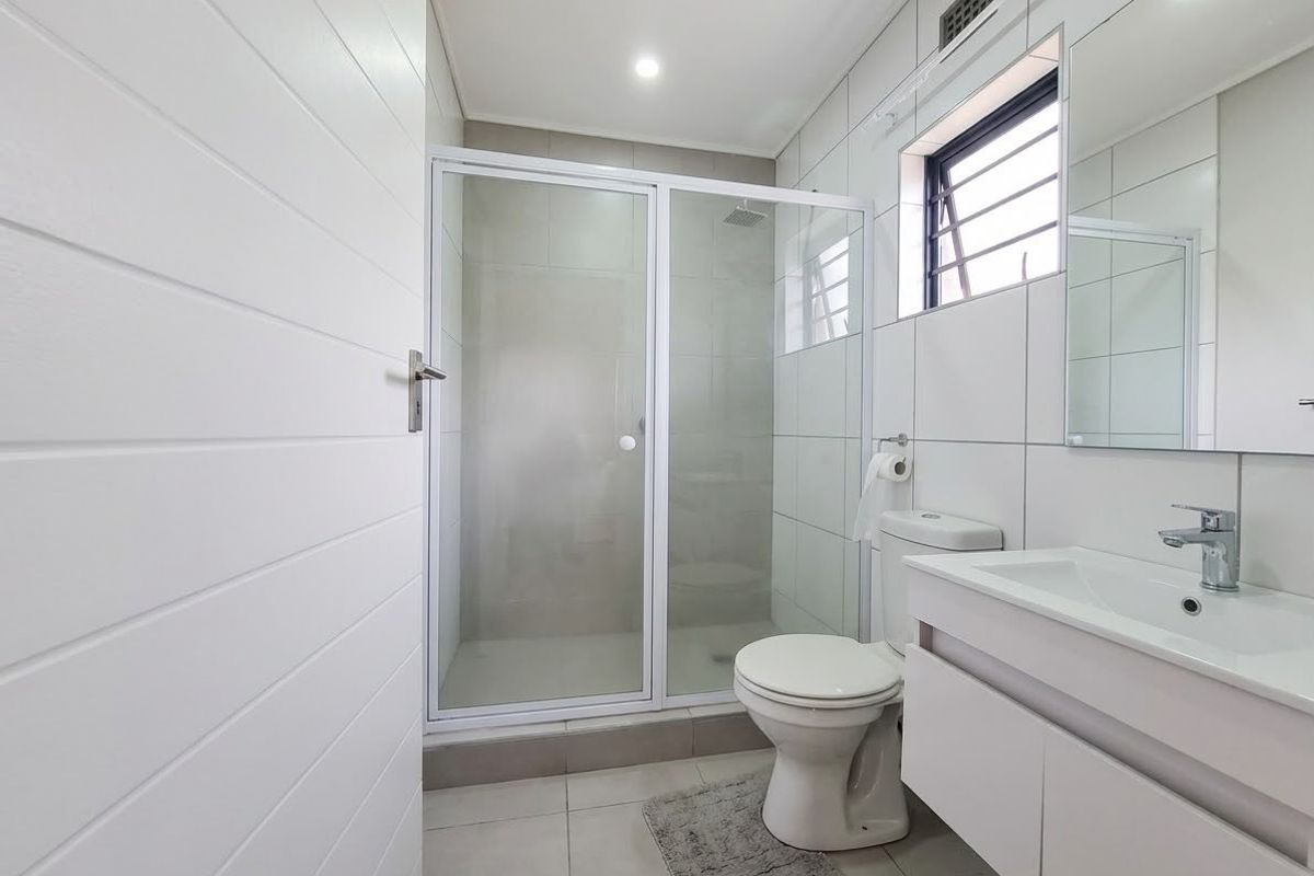 A clean, modern bathroom featuring a glass-enclosed shower, wall-mounted vanity with basin, and neutral tiled finishes throughout.