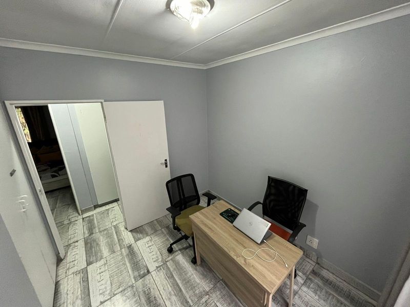 A functional office space featuring modern wood-look tiled flooring, neutral grey walls, and a simple ceiling light fixture.