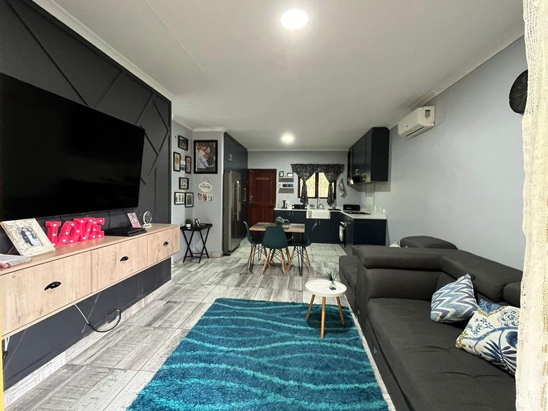 An open-plan living and kitchen area featuring modern dark cabinetry, tiled flooring, and a split-system air conditioner, creating a functional and cohesive living space.