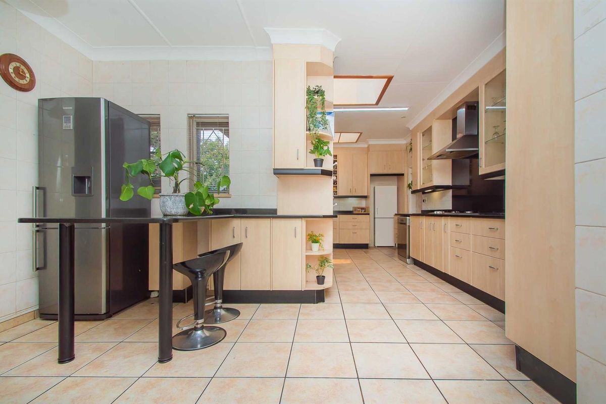 Spacious kitchen featuring light wood cabinetry, dark countertops, tiled flooring, and integrated appliances, offering ample storage and a functional layout.