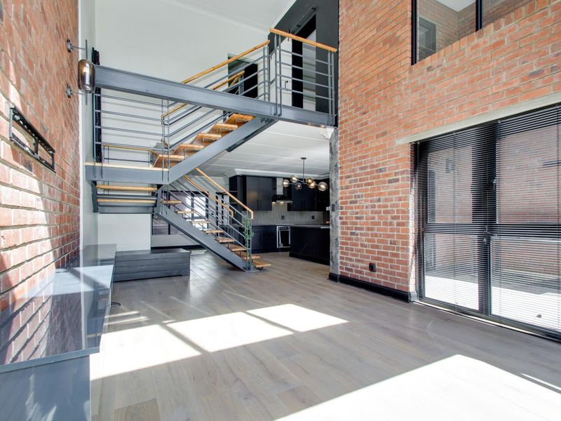 Spacious open-plan living area featuring industrial-style exposed brick walls, a striking steel staircase, and a modern kitchen with integrated appliances.