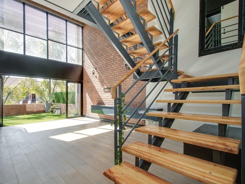 Spacious living area featuring a striking exposed brick wall, modern timber staircase, and large bi-fold doors opening to a private garden.