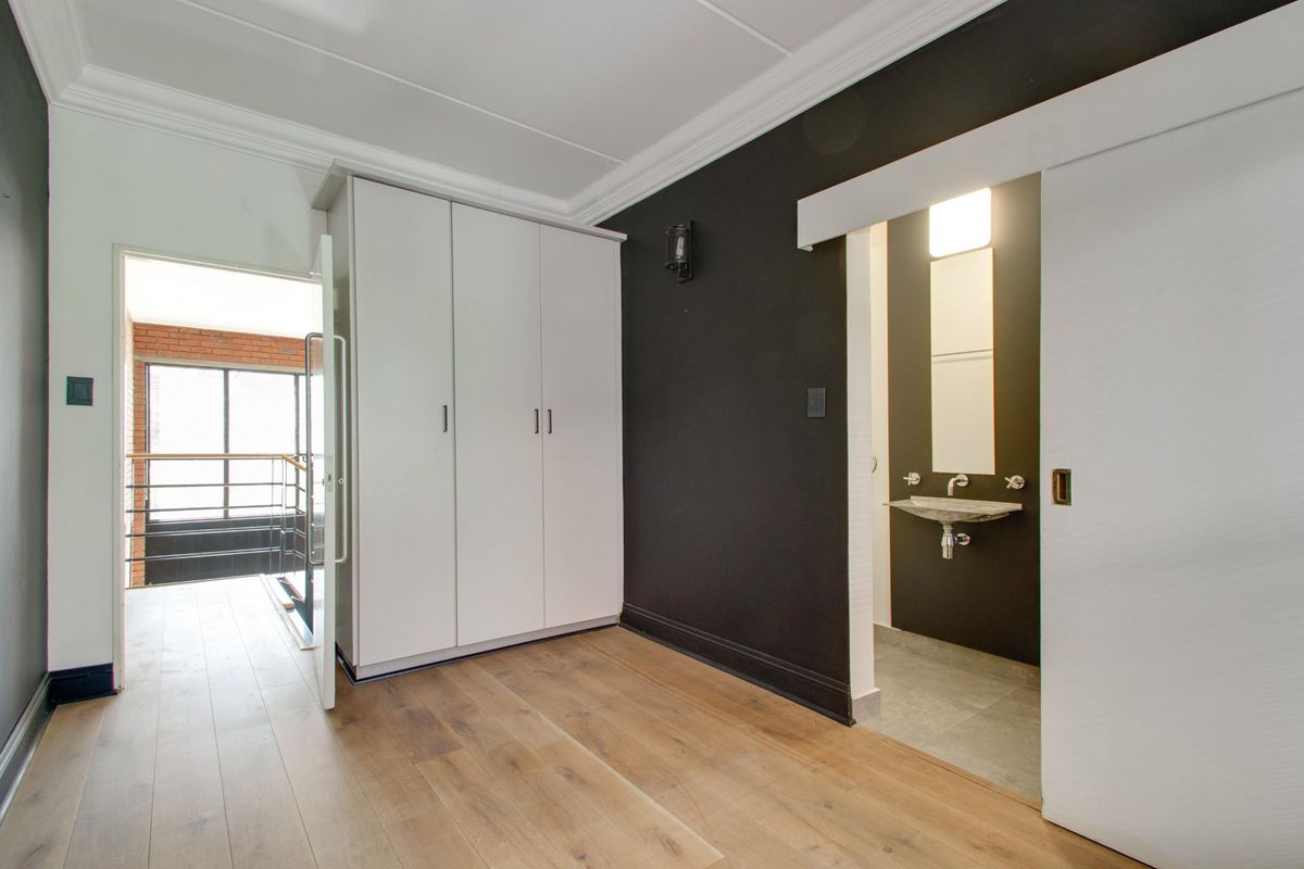 A bright bedroom featuring laminate flooring, built-in cupboards, and a modern en-suite vanity area with a sliding door entrance.