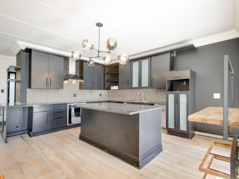 Modern kitchen featuring dark cabinetry, granite countertops, a central island, built-in oven, extractor fan, and light-toned laminate flooring.