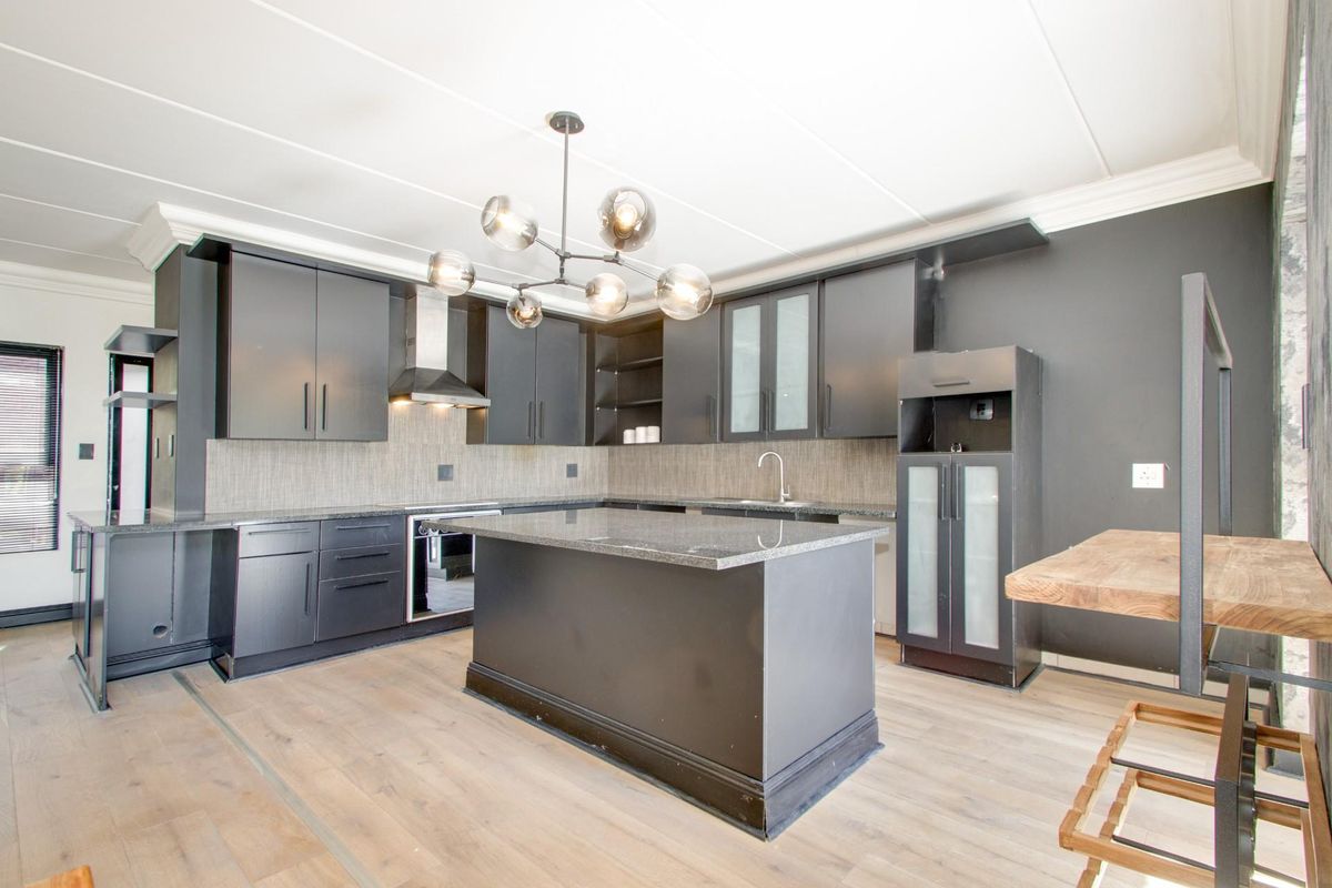Modern kitchen featuring dark cabinetry, granite countertops, a central island, built-in oven, extractor fan, and light-toned laminate flooring.