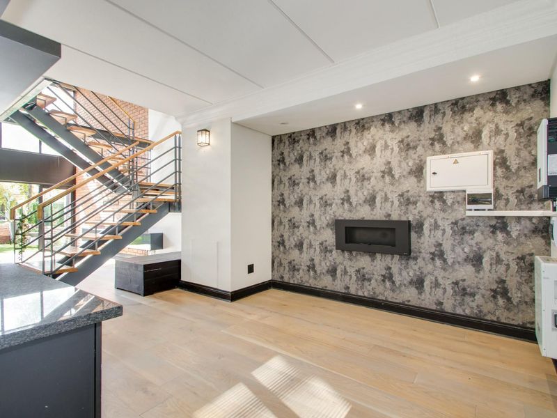 Spacious open-plan living area featuring modern timber flooring, a striking metal staircase, built-in fireplace, and integrated electrical and inverter infrastructure.
