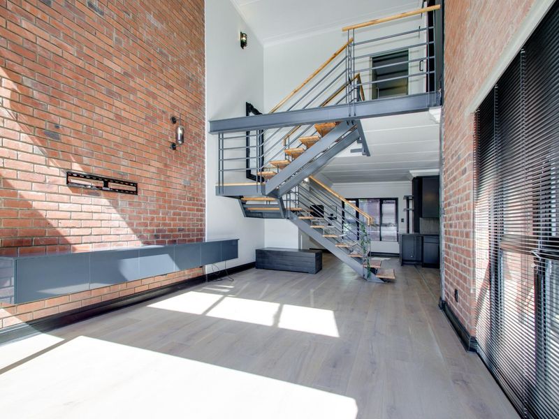 Spacious industrial-style living area featuring exposed brick walls, high ceilings, and a striking steel staircase with timber treads.