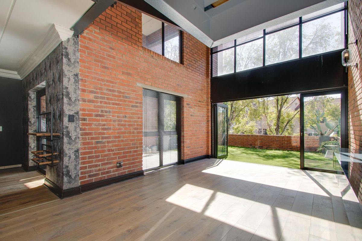 Spacious living area featuring exposed brick walls, high ceilings with clerestory windows, and bi-fold doors opening onto a private garden.