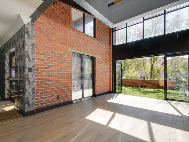 Spacious living area featuring exposed brick walls, high ceilings with clerestory windows, and bi-fold doors opening onto a private garden.