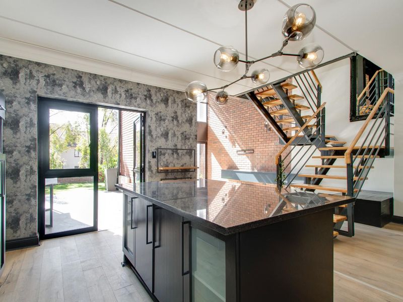Modern open-plan living area featuring a sleek kitchen island, exposed brick wall, and a contemporary staircase leading to the upper level.