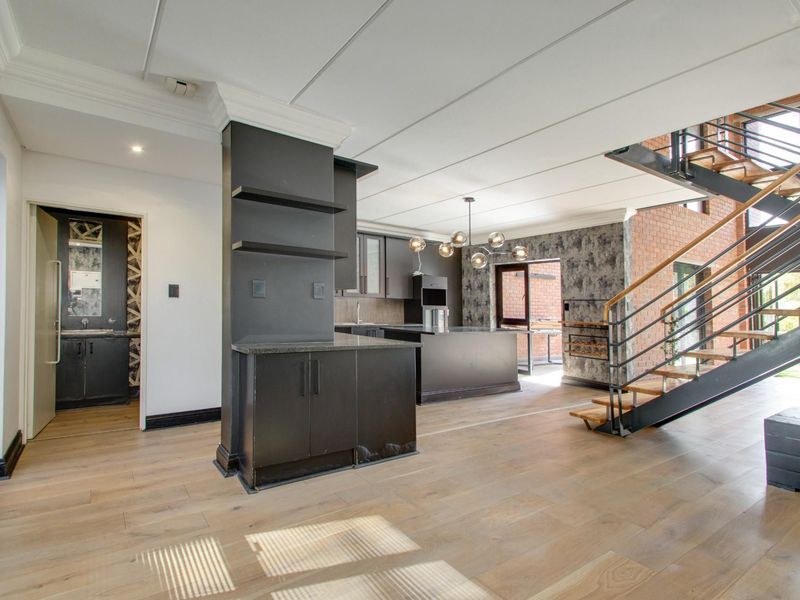 Spacious open-plan living area featuring a modern kitchen with island, exposed brick accents, and a striking staircase leading to the upper level.