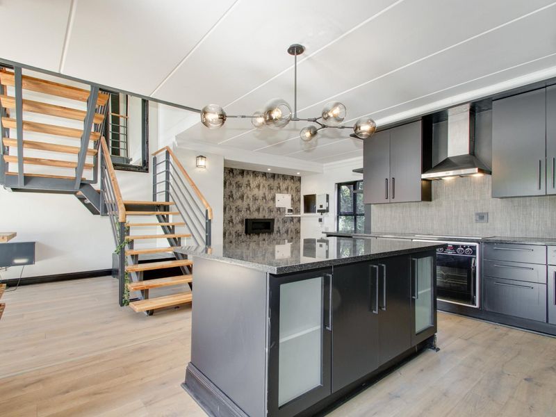 Modern open-plan kitchen featuring a central island, sleek cabinetry, built-in appliances, and a striking industrial-style staircase leading to the upper level.