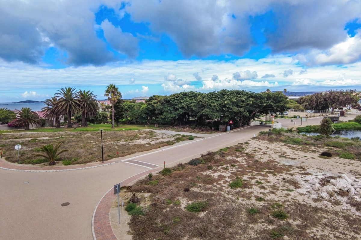 Aerial view of a vacant residential plot featuring paved road access, established trees, and surrounding landscape in a coastal estate setting.