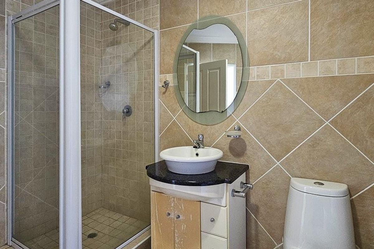 A compact bathroom featuring a glass-enclosed shower, a vessel sink vanity with stone countertop, and a standard toilet, finished with neutral wall tiles.