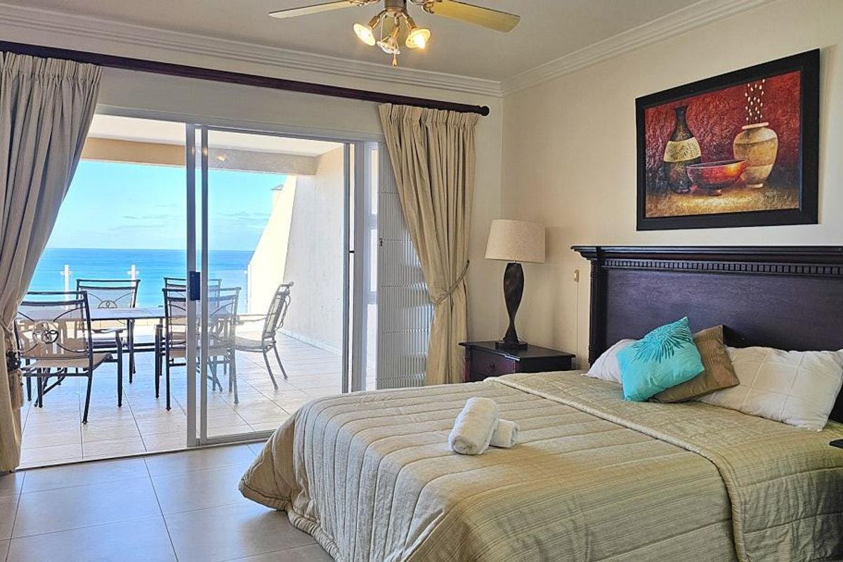 Spacious bedroom featuring tiled flooring, a ceiling fan, and large sliding glass doors opening onto a private balcony with ocean views.