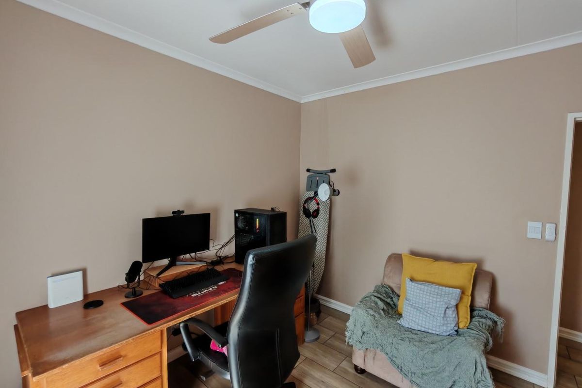 A functional bedroom space currently utilized as a home office, featuring tiled flooring, neutral wall paint, and a ceiling fan.