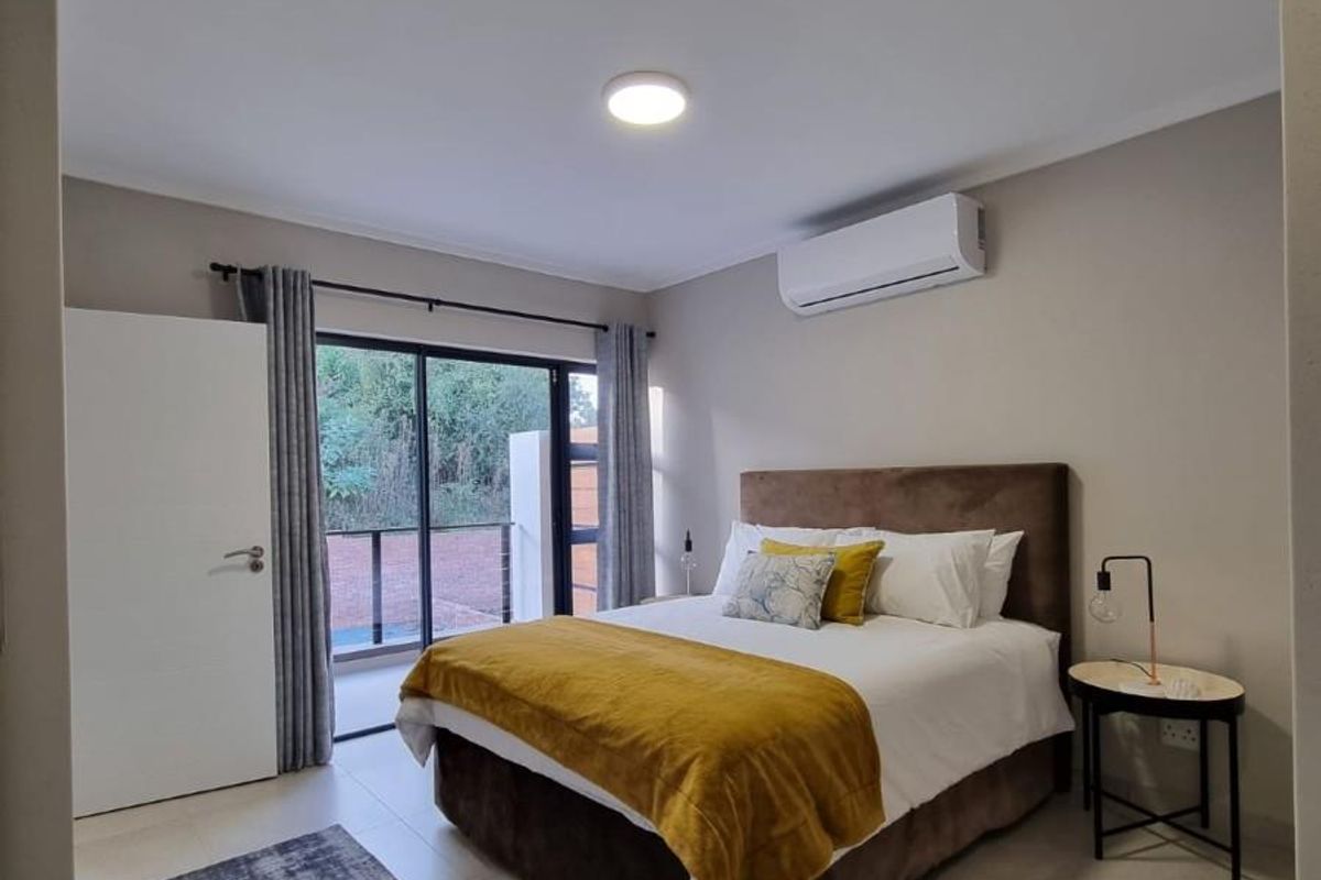 A well-maintained bedroom featuring neutral wall tones, tiled flooring, a wall-mounted air conditioning unit, and sliding glass doors leading to an outdoor balcony.