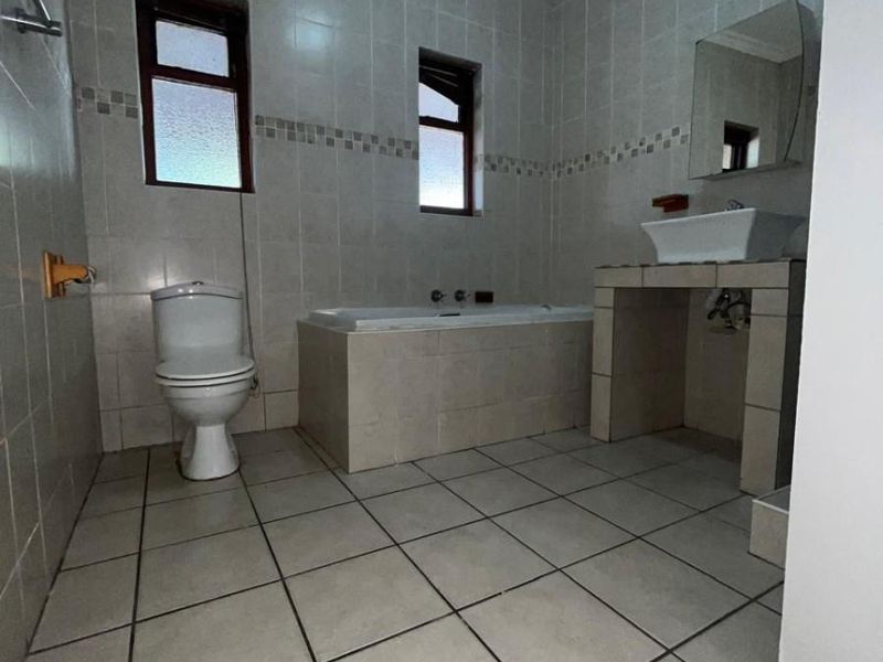 A functional bathroom featuring a built-in bathtub, a vessel sink on a tiled vanity, and a standard toilet with neutral wall and floor tiling.