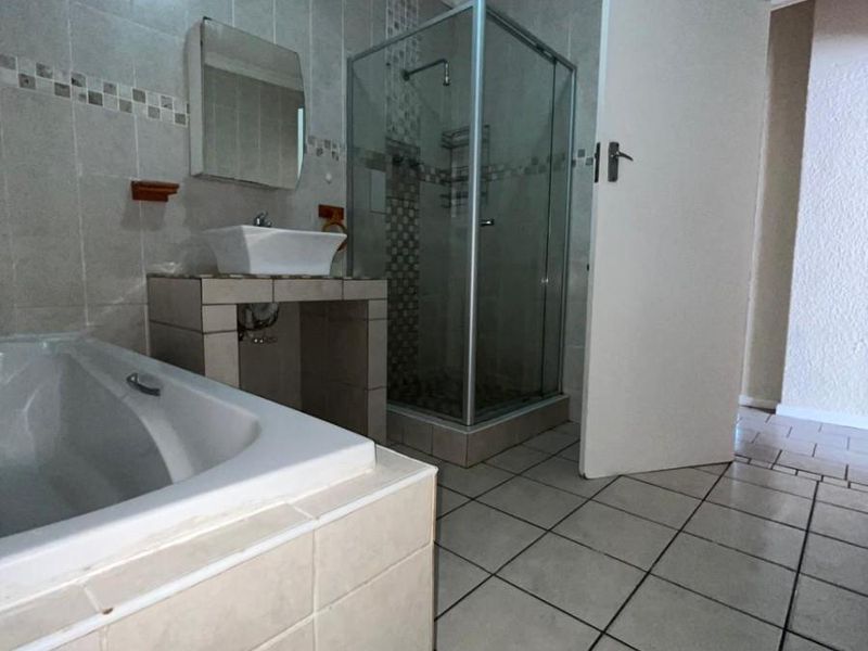 A functional bathroom featuring a tiled bathtub, a separate glass-enclosed shower, and a modern vessel sink vanity with wall-mounted mirror.