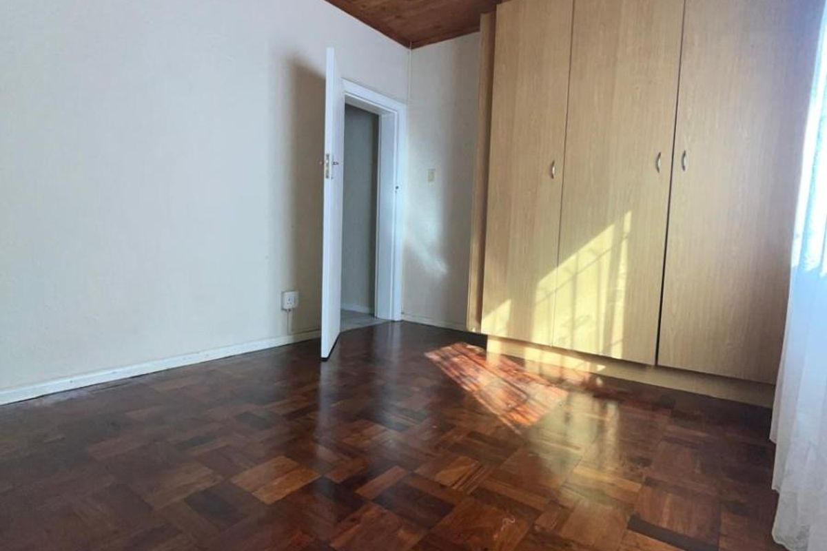A bedroom featuring classic parquet flooring, a timber-paneled ceiling with a fitted fan, and built-in wooden cabinetry.