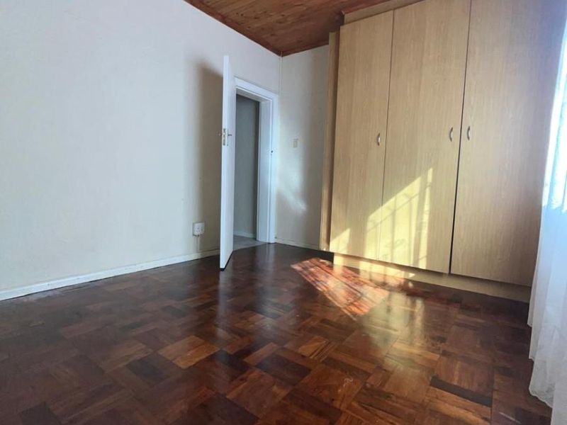 A bedroom featuring classic parquet flooring, a timber-paneled ceiling with a fitted fan, and built-in wooden cabinetry.