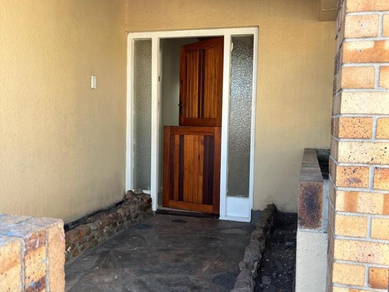Covered front entrance featuring a rustic stable-style wooden door, stone paved flooring, and brick planter boxes.