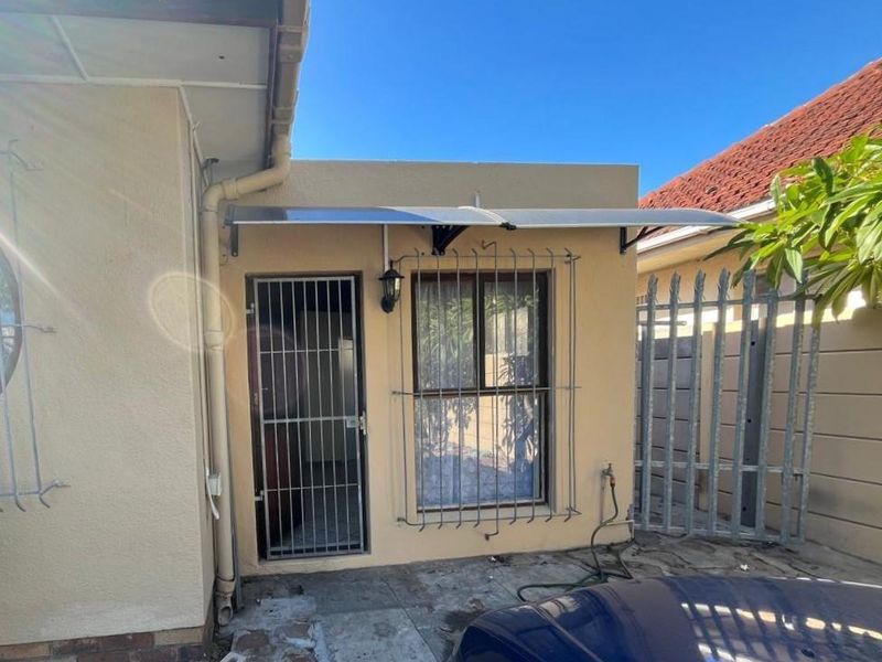 Exterior view of the property side entrance featuring a security gate, window security bars, and a protective awning over the doorway.