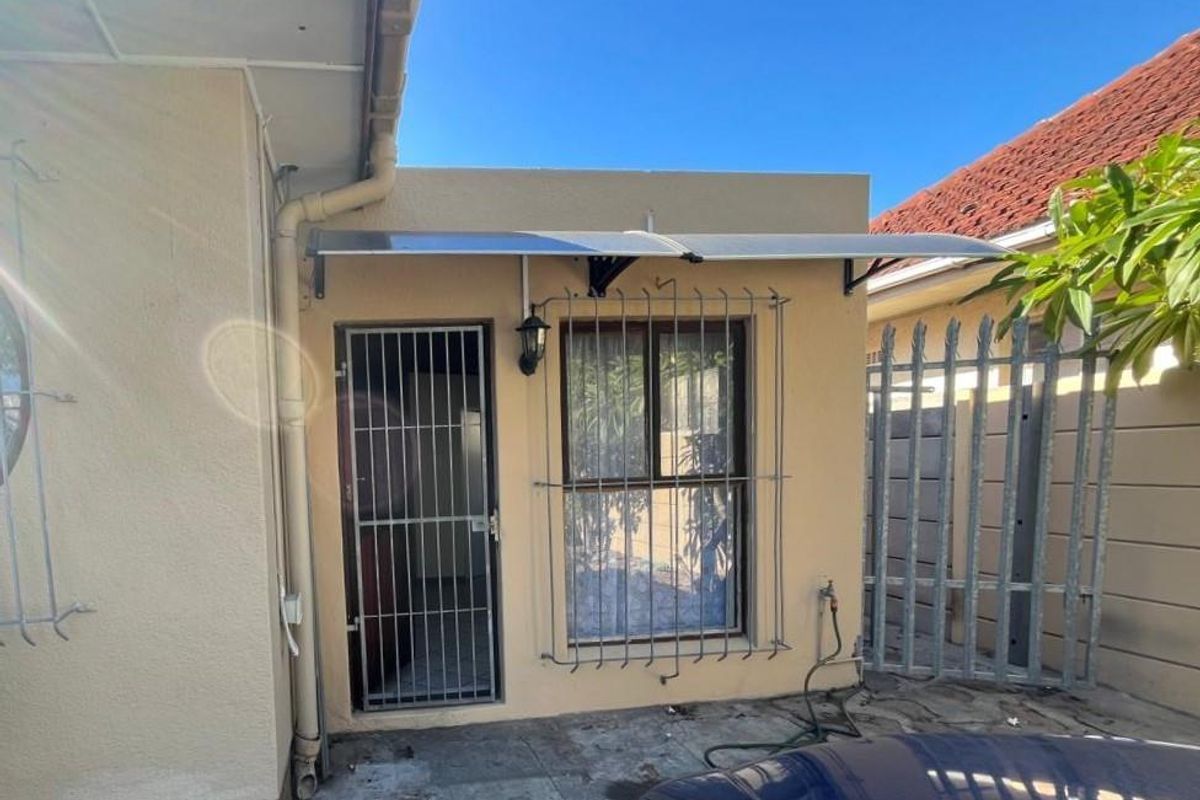 Exterior view of the property side entrance featuring a security gate, window security bars, and a protective awning over the doorway.
