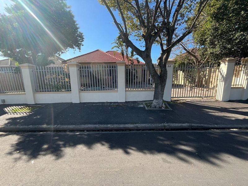 Front view of the property featuring a secure perimeter wall with metal palisade fencing and a gated driveway entrance.